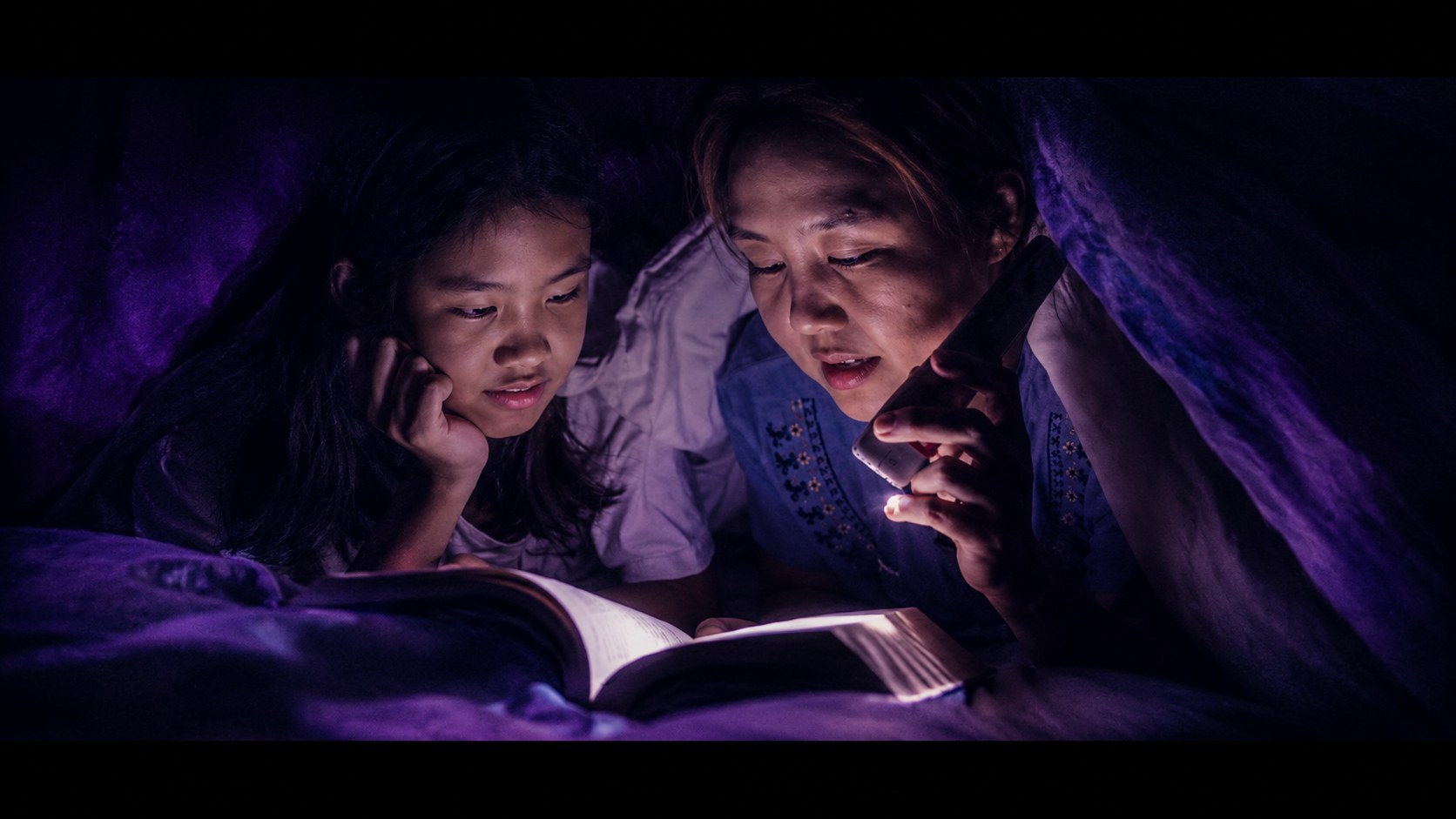 A mother and child reading together by lamplight
